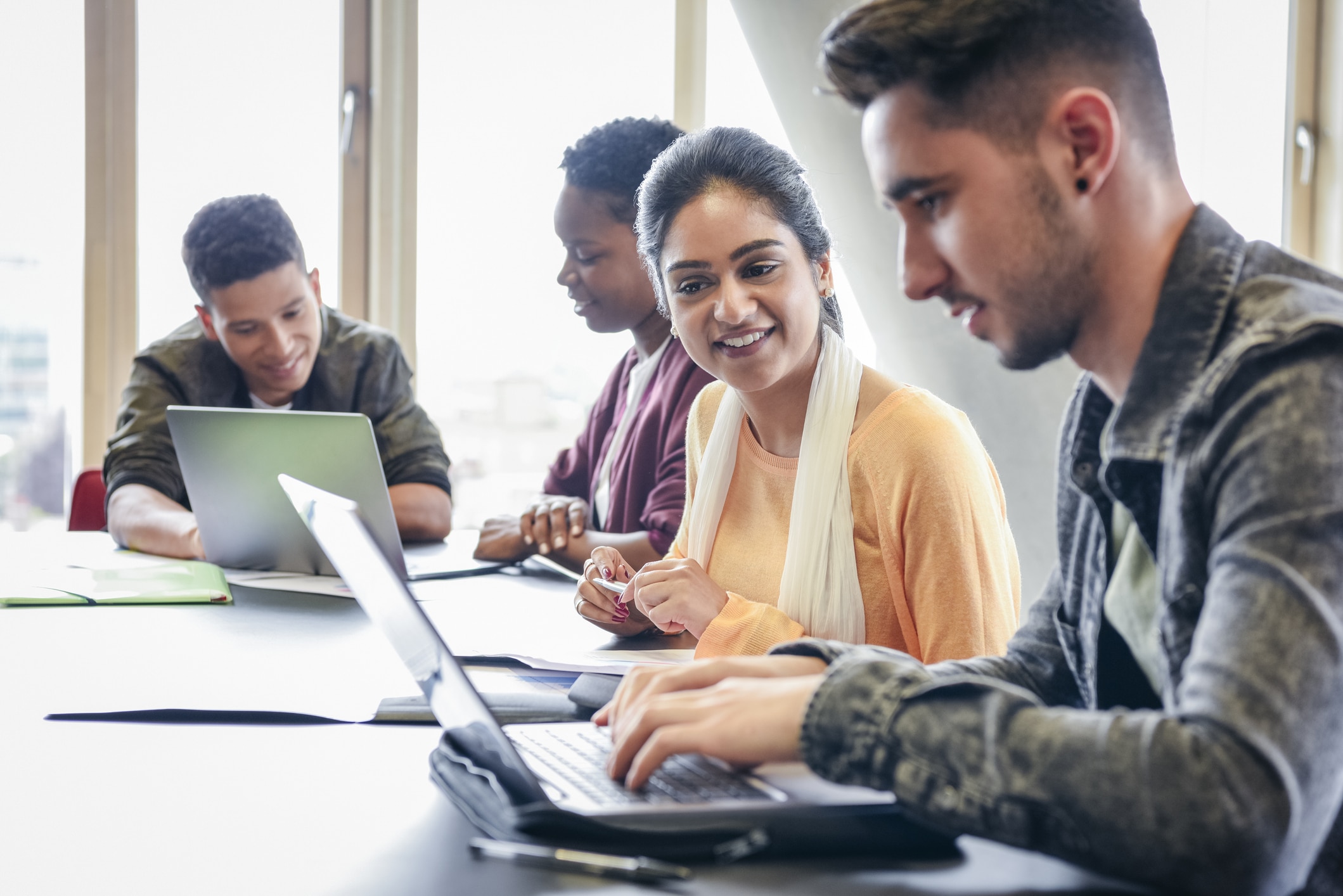 Young man using laptop with female student watching and smiling College students working on computer in classroom, young adults in further education, man concentrating as he types on keyboard